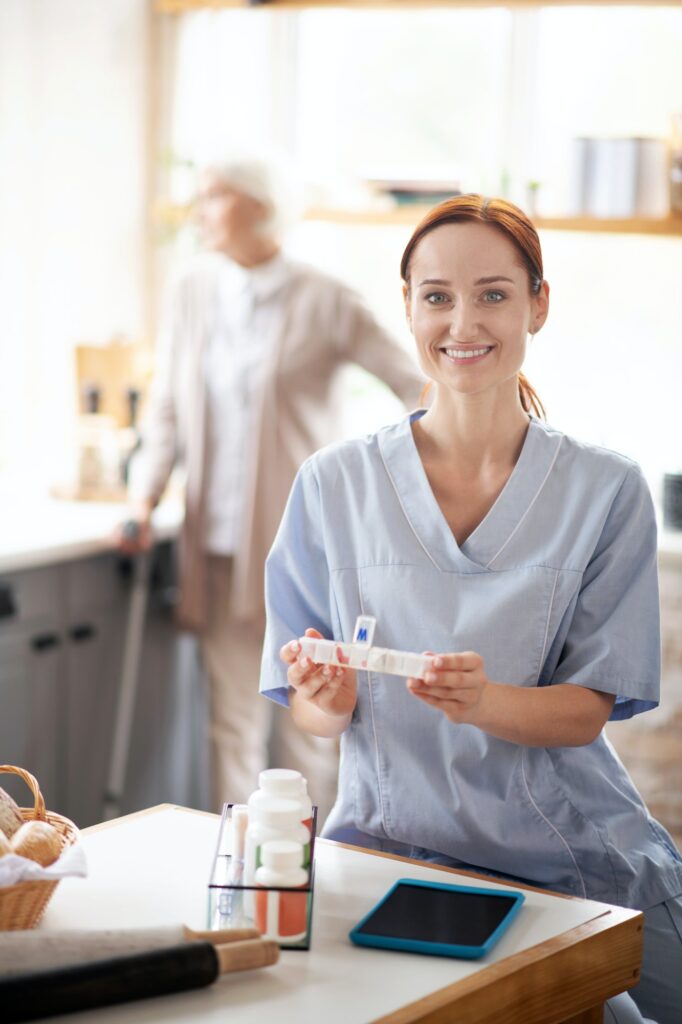 Young caregiver wearing uniform holding box with pills